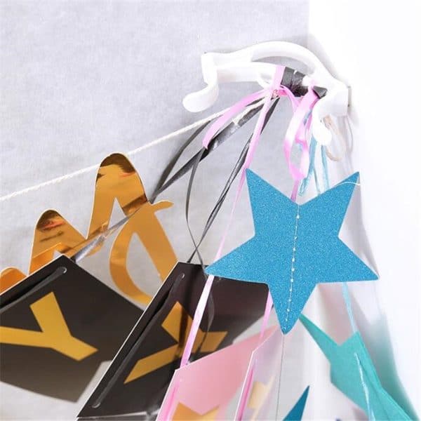 slingerklem gepositioneerd tussen de hoek van 2 muren, waaraan 5 uiteindes van slingers te zien zijn in de kleuren goud, zwart, roze en blauw