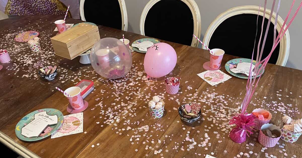Feestelijk gedekte babyshower tafel met roze confetti, ballonnen, Hello-servetjes en invulkaartjes
