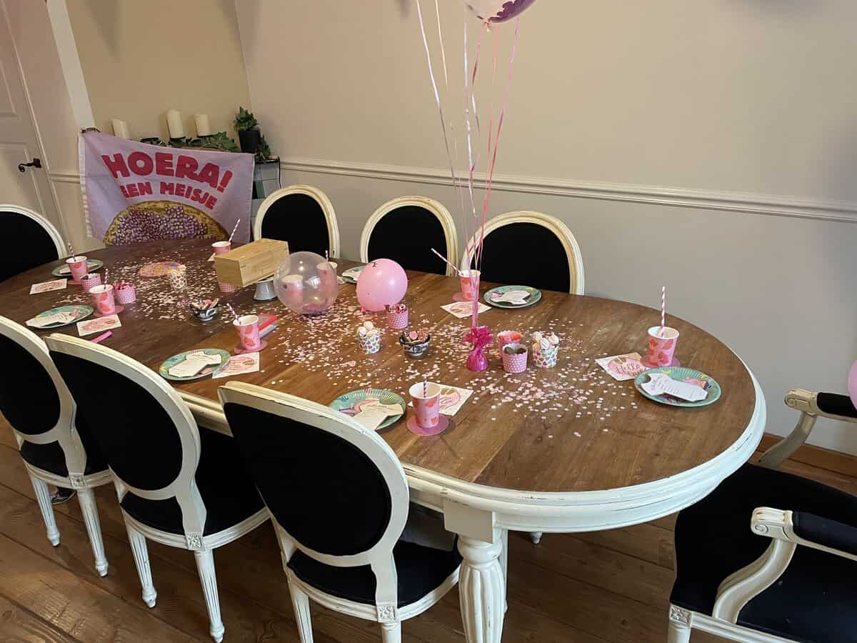 Babyshower thuis aan de eettafel met roze versiering, ballonnen en een Hoera een meisje vlag