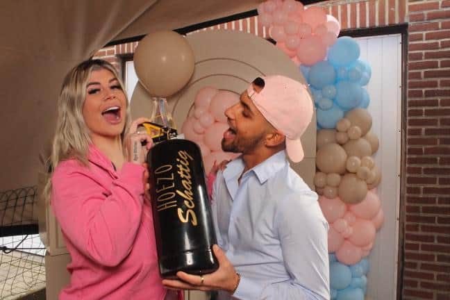Lachend stel houdt een HoezoSchattig gender reveal brandblusser vast voor een roze en blauwe ballonboog