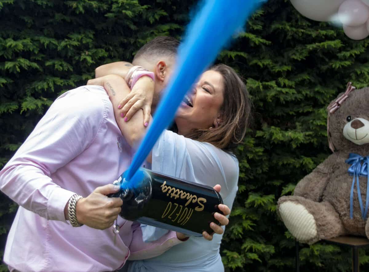 Aanstaande ouders omhelzen elkaar terwijl een HoezoSchattig gender reveal brandblusser blauw poeder spuit