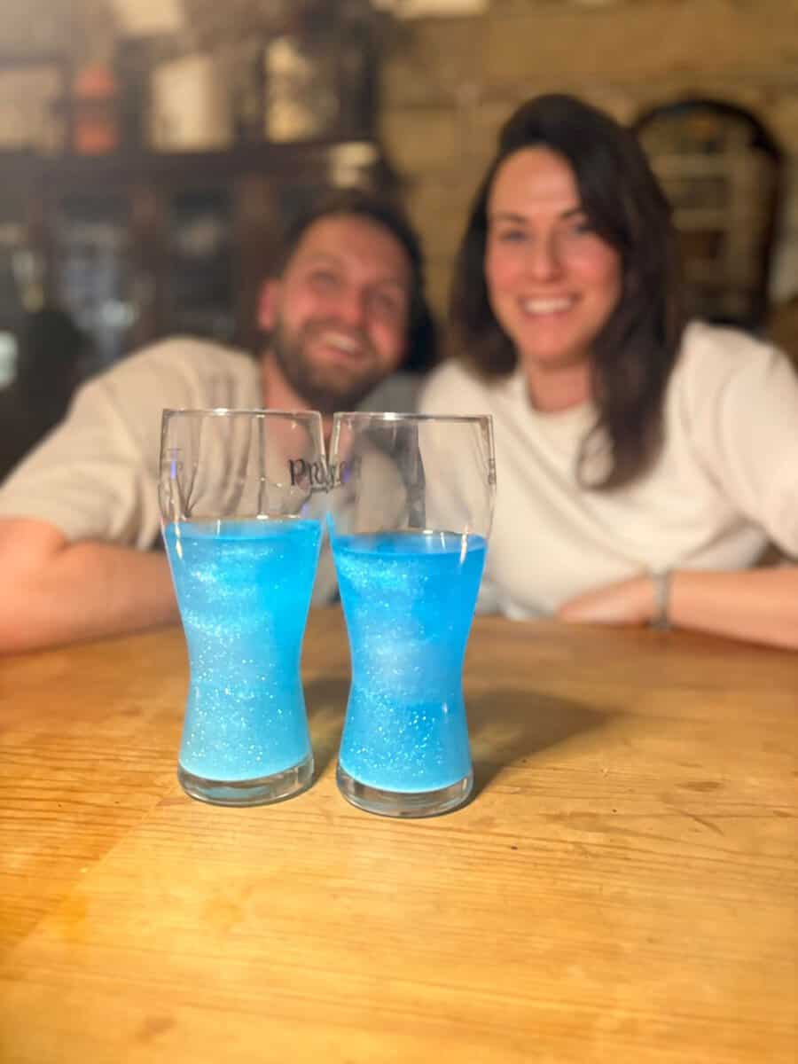 Twee glazen met blauw glinsterend gender reveal drinkpoeder voor een lachend stel