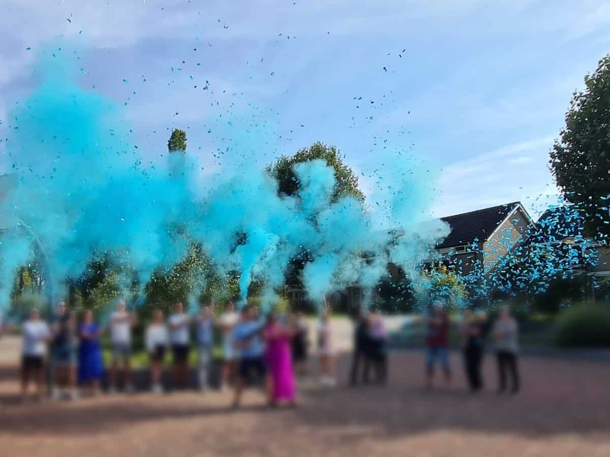Groep gasten schiet tegelijk blauwe confetti en rook de lucht in bij een gender reveal